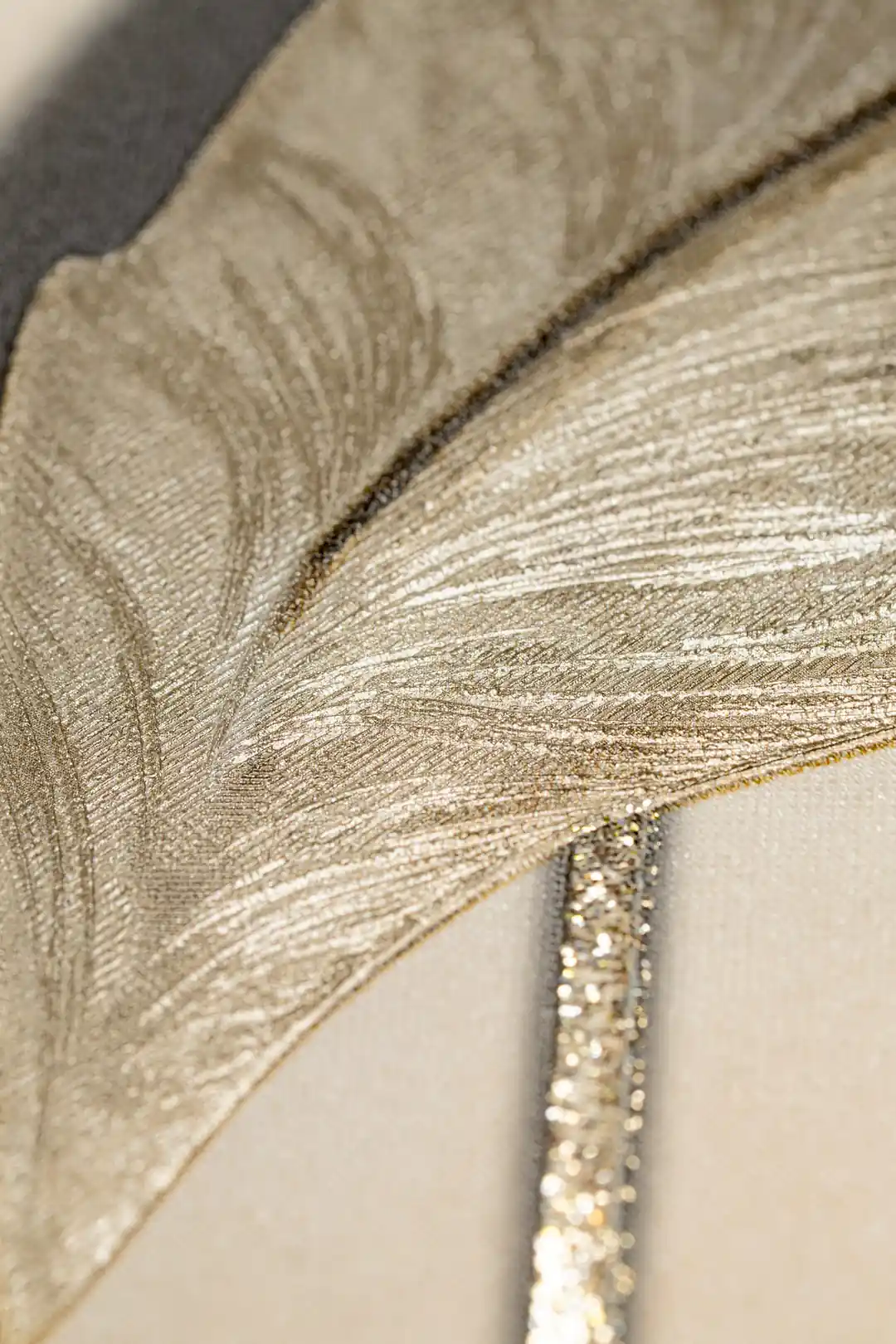 Extreme macro of an embossed leaf showing champagne-toned veins and fine textured detail on cream wallpaper