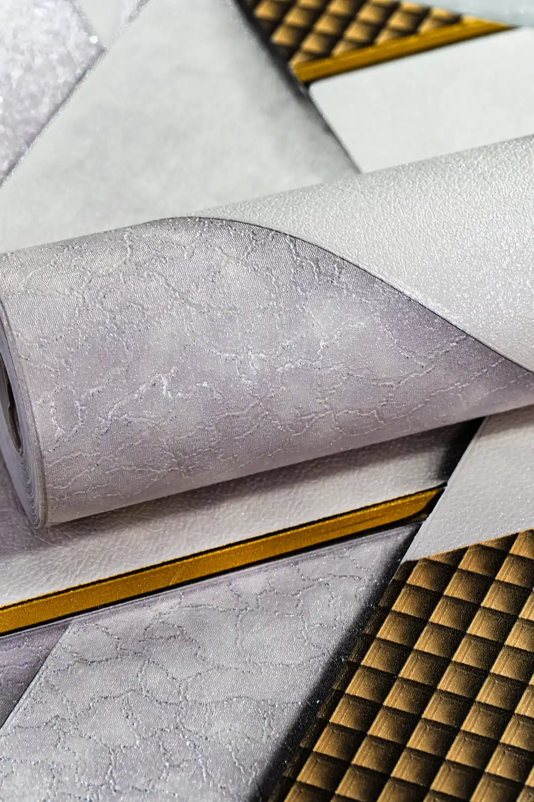 White and grey geometric wallpaper roll with metallic gold grid lines and 3D triangular pattern design
