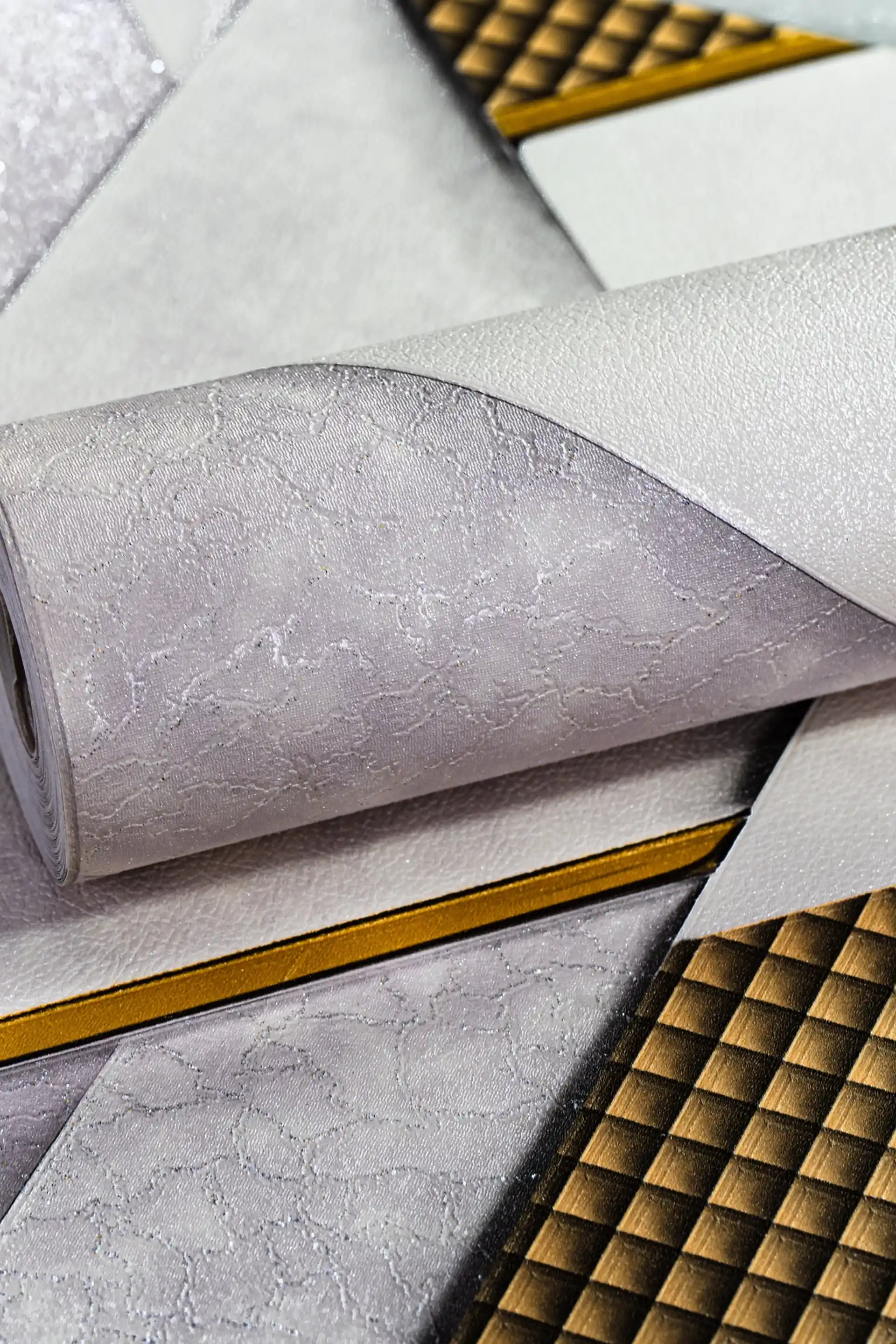 White and grey geometric wallpaper roll with metallic gold grid lines and 3D triangular pattern design