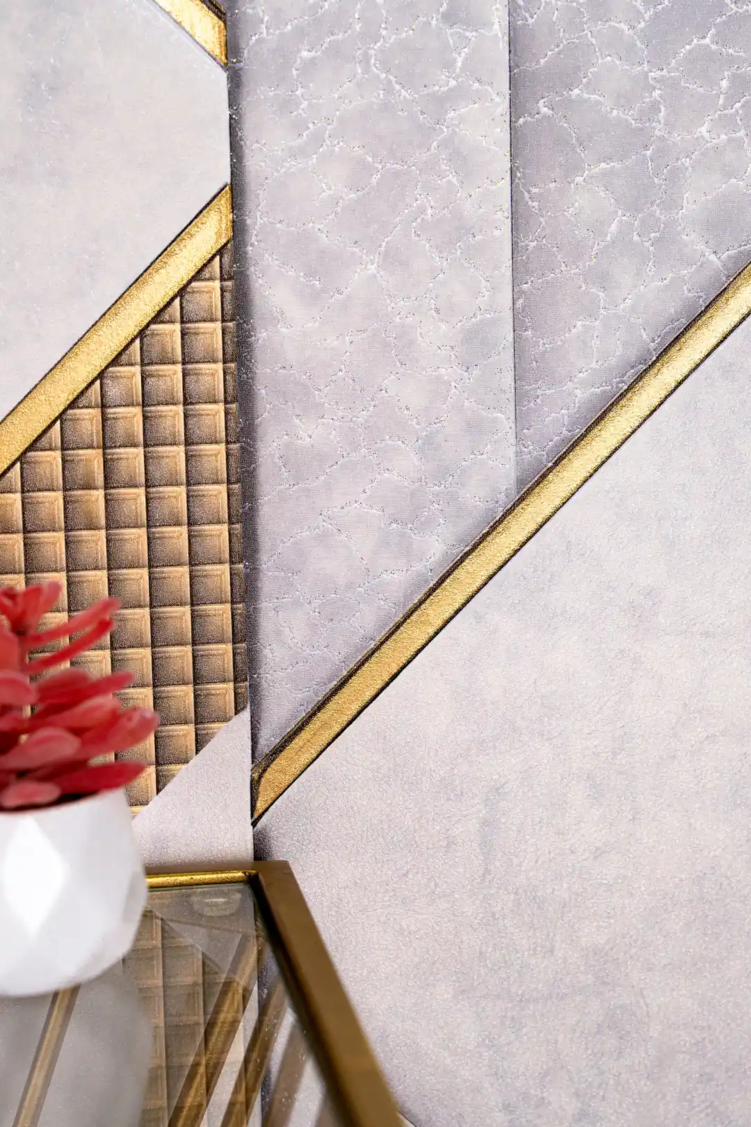 Detailed view of metallic gold quilted grid panels and textured grey marble surfaces on geometric wallpaper with red flowers in foreground