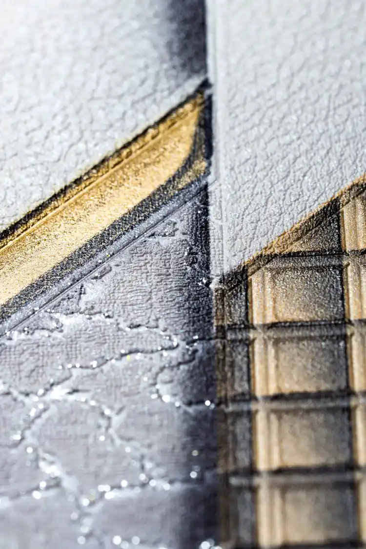 Extreme macro showing gold metallic quilted grid texture meeting grey textured surface on embossed geometric wallpaper