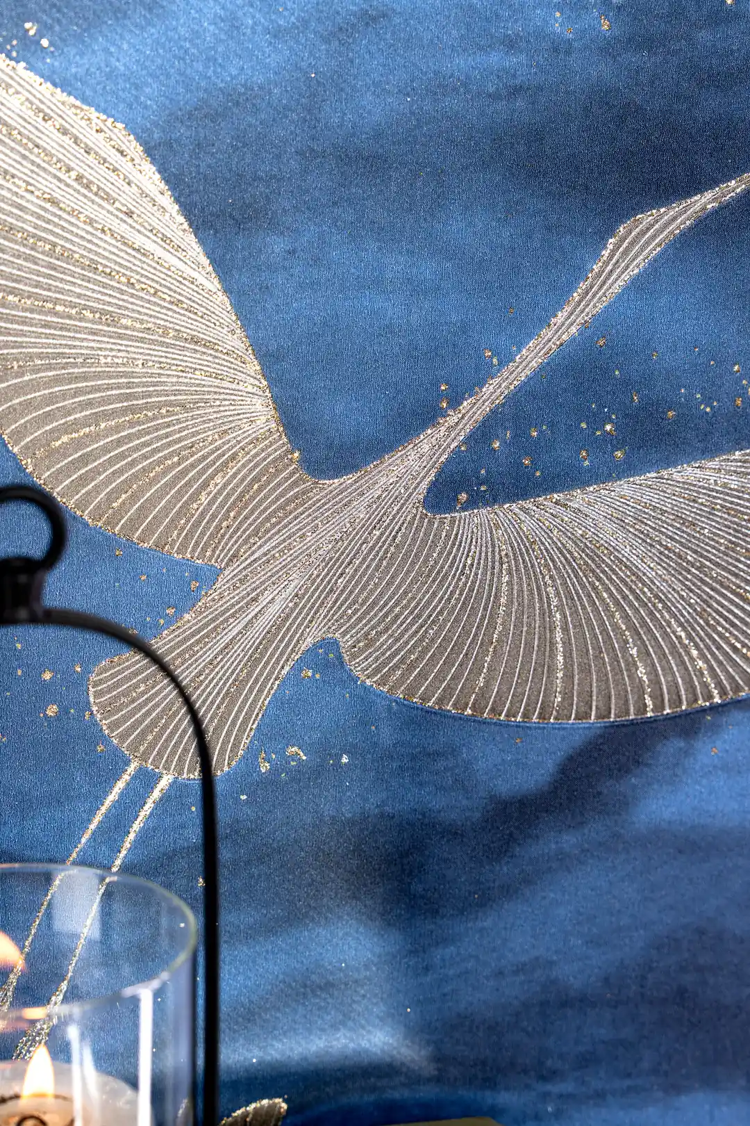 Detailed view of a silver crane in flight with embossed wing texture next to a hanging lantern on blue wall