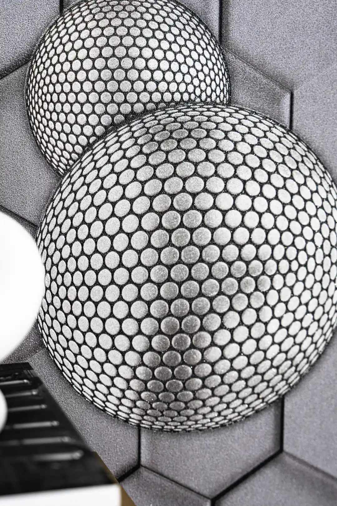 Close-up of two overlapping 3D textured spheres with circular dot pattern on grey hexagon wallpaper background