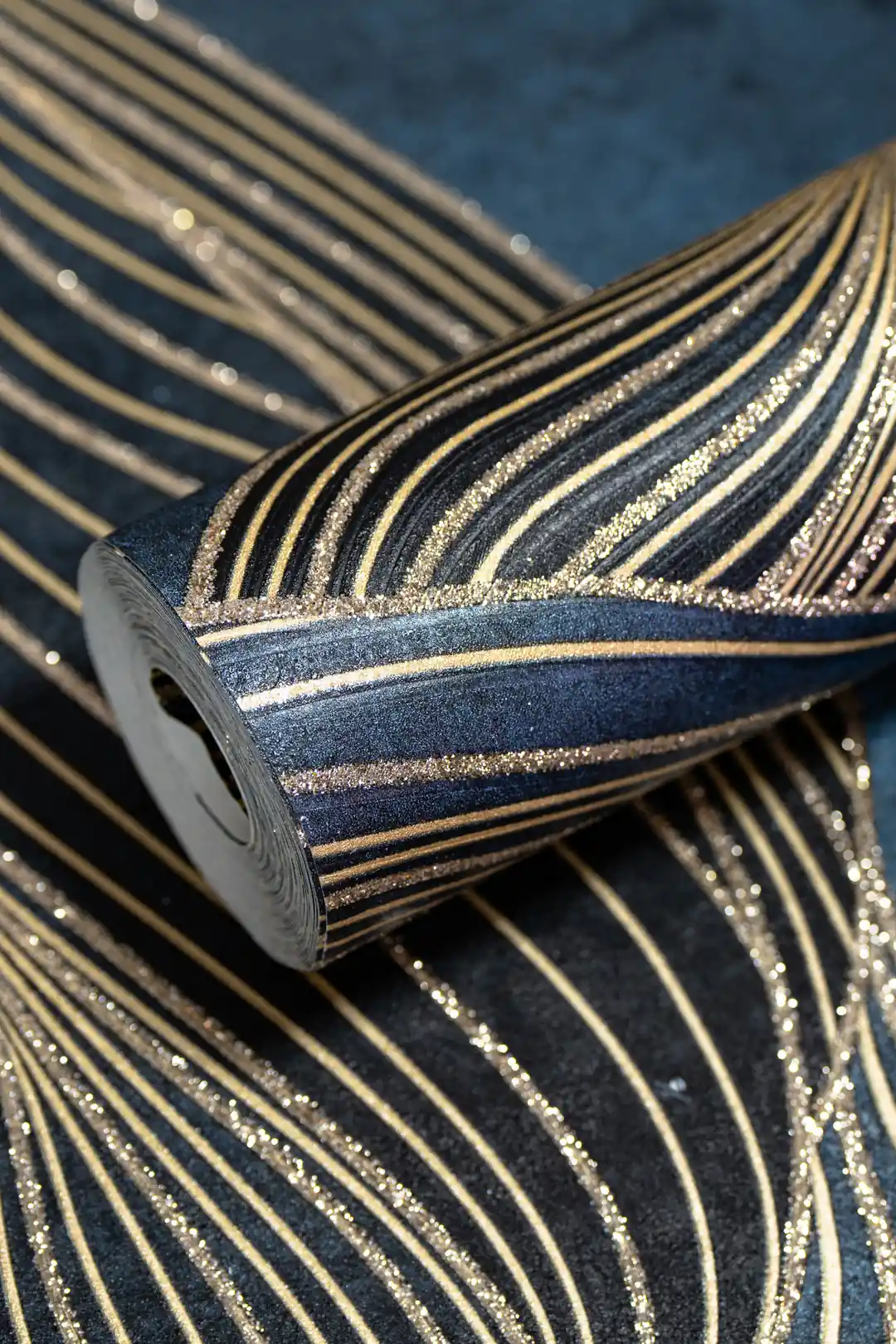 Rolled dark navy wallpaper with flowing gold swirl lines and glitter accents on textured blue surface