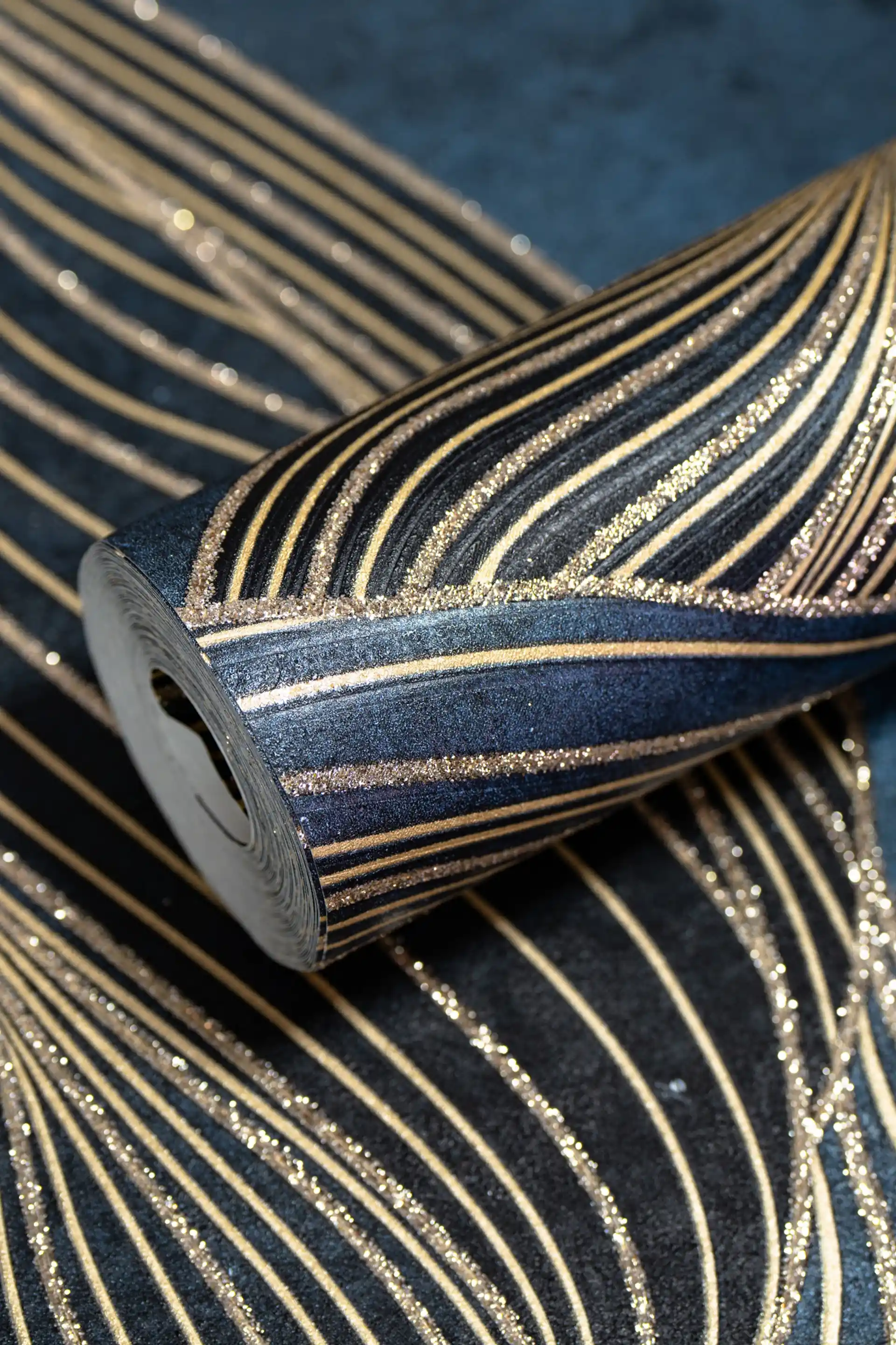 Rolled dark navy wallpaper with flowing gold swirl lines and glitter accents on textured blue surface