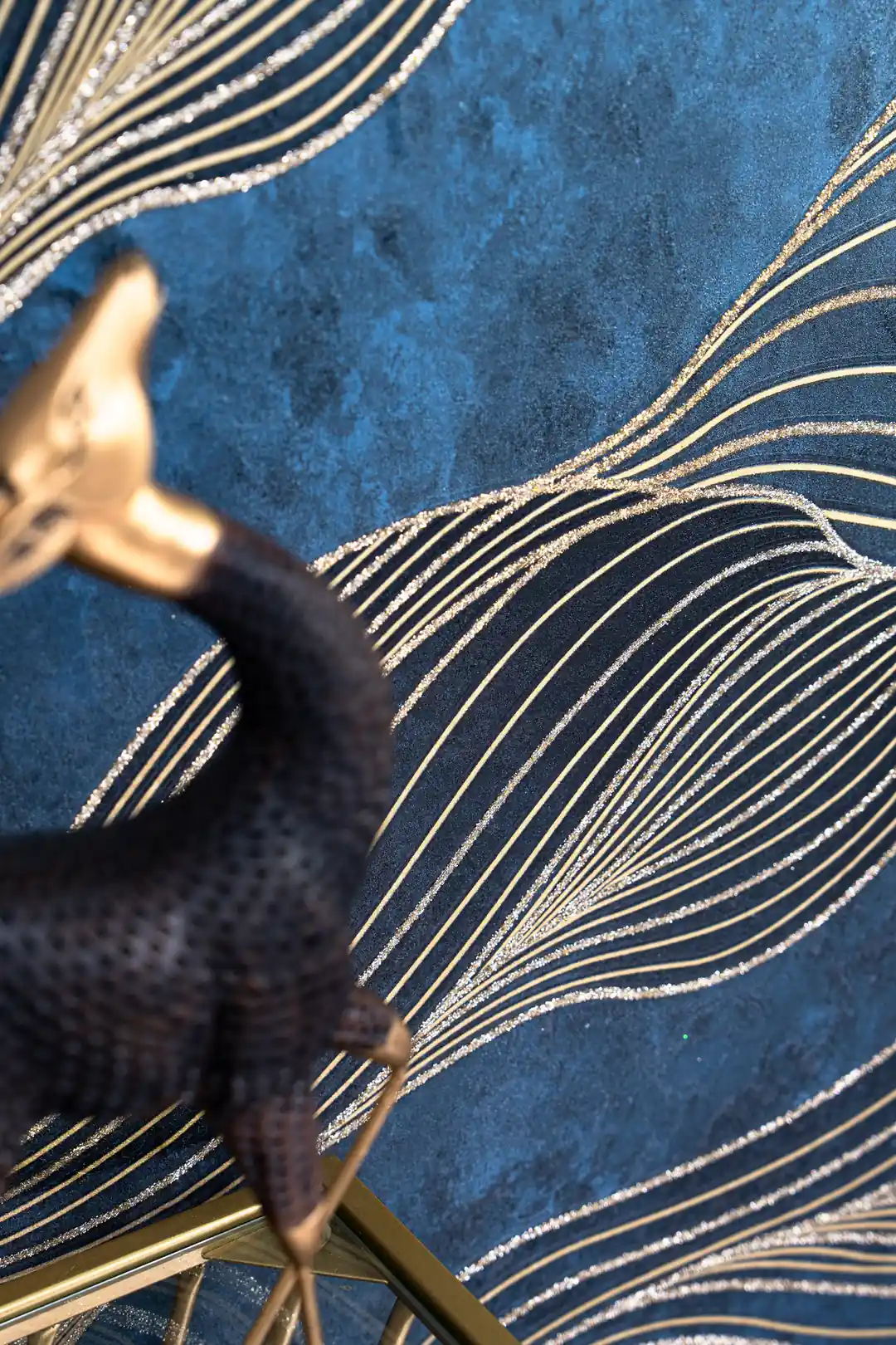 Close-up of gold flowing wave pattern on dark navy wallpaper with a decorative dark bronze bird figurine