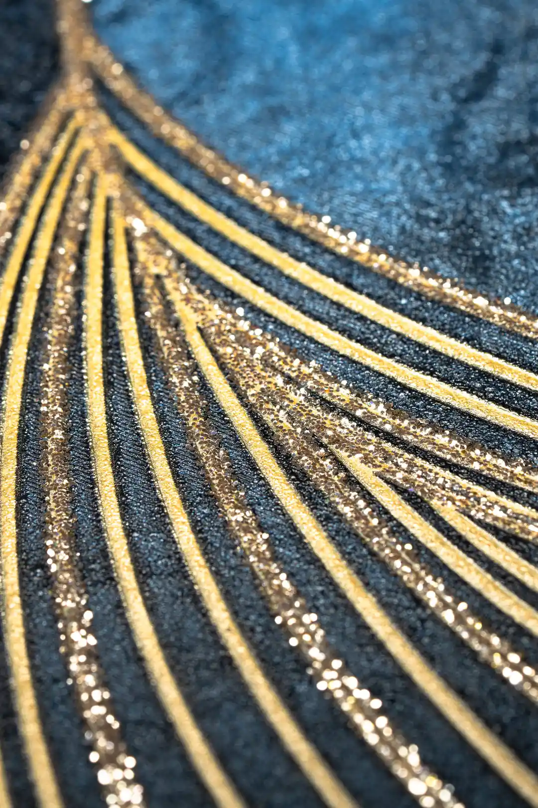 Extreme close-up of gold glitter swirl lines radiating outward on dark navy textured wallpaper surface