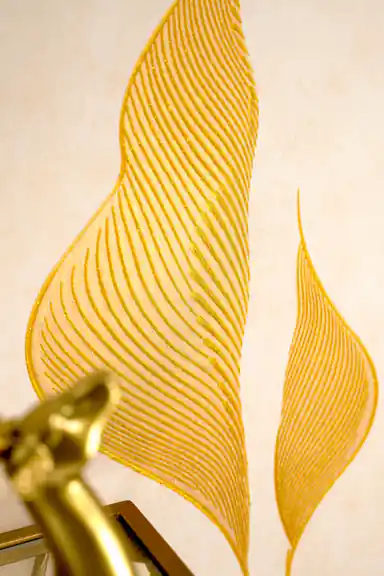 Close-up of embossed gold lily petal with detailed line striations next to a gold lamp fixture