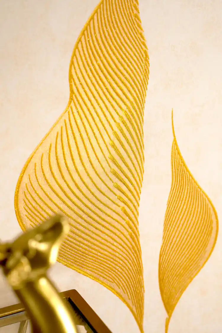 Close-up of embossed gold lily petal with detailed line striations next to a gold lamp fixture