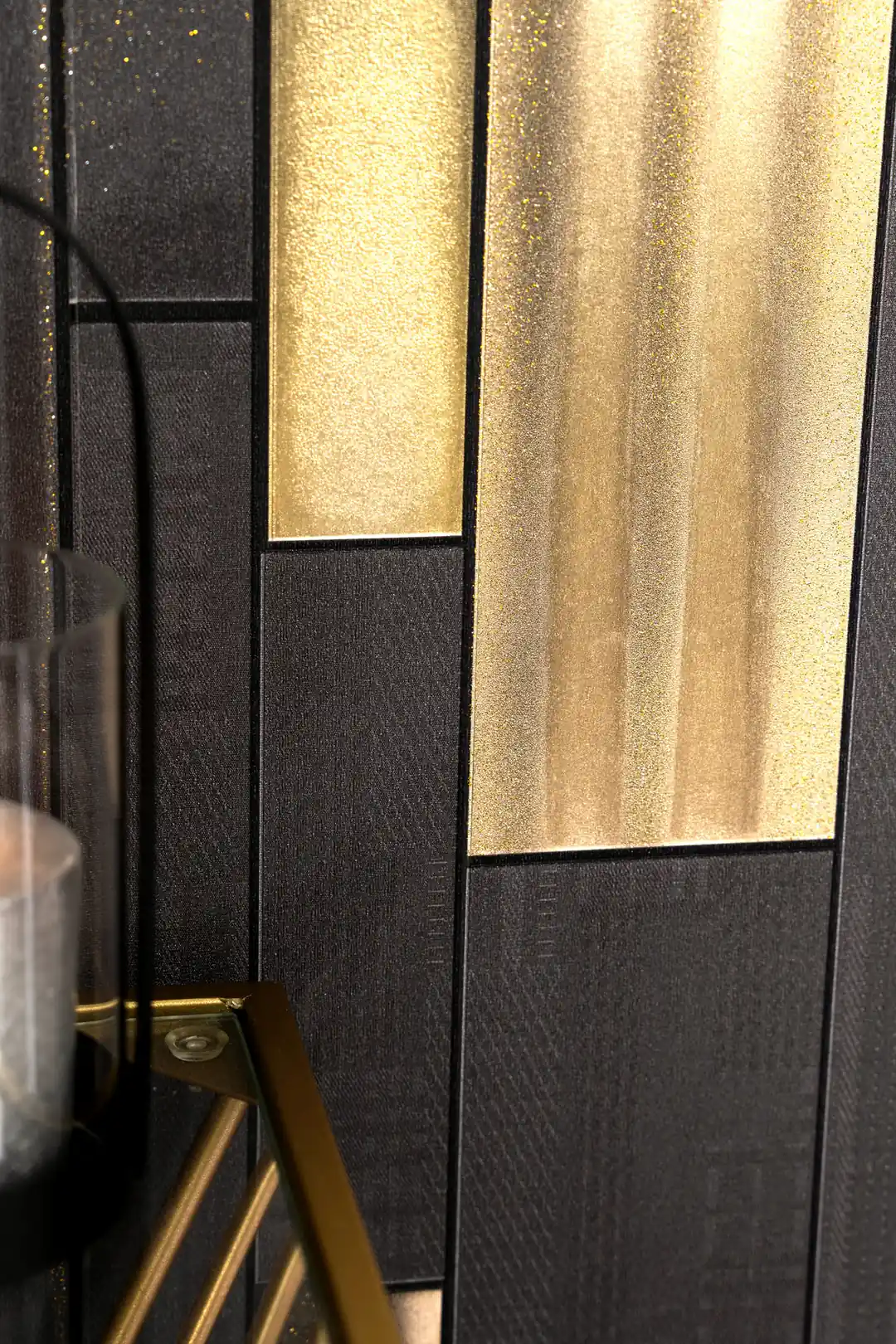 Detail view of gold metallic panel and textured charcoal surface with glitter accents beside a glass candle