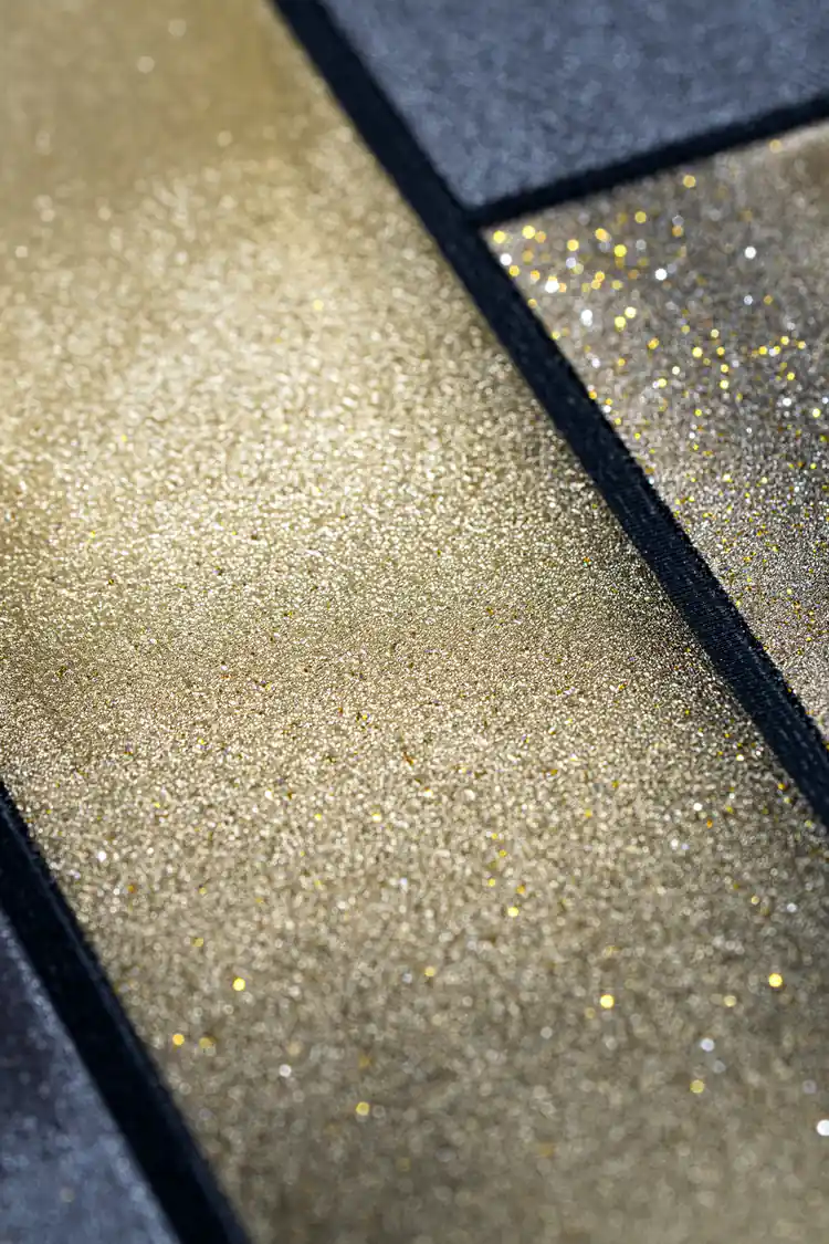 Extreme close-up macro of gold glitter panel surface meeting dark charcoal textured wallpaper edge