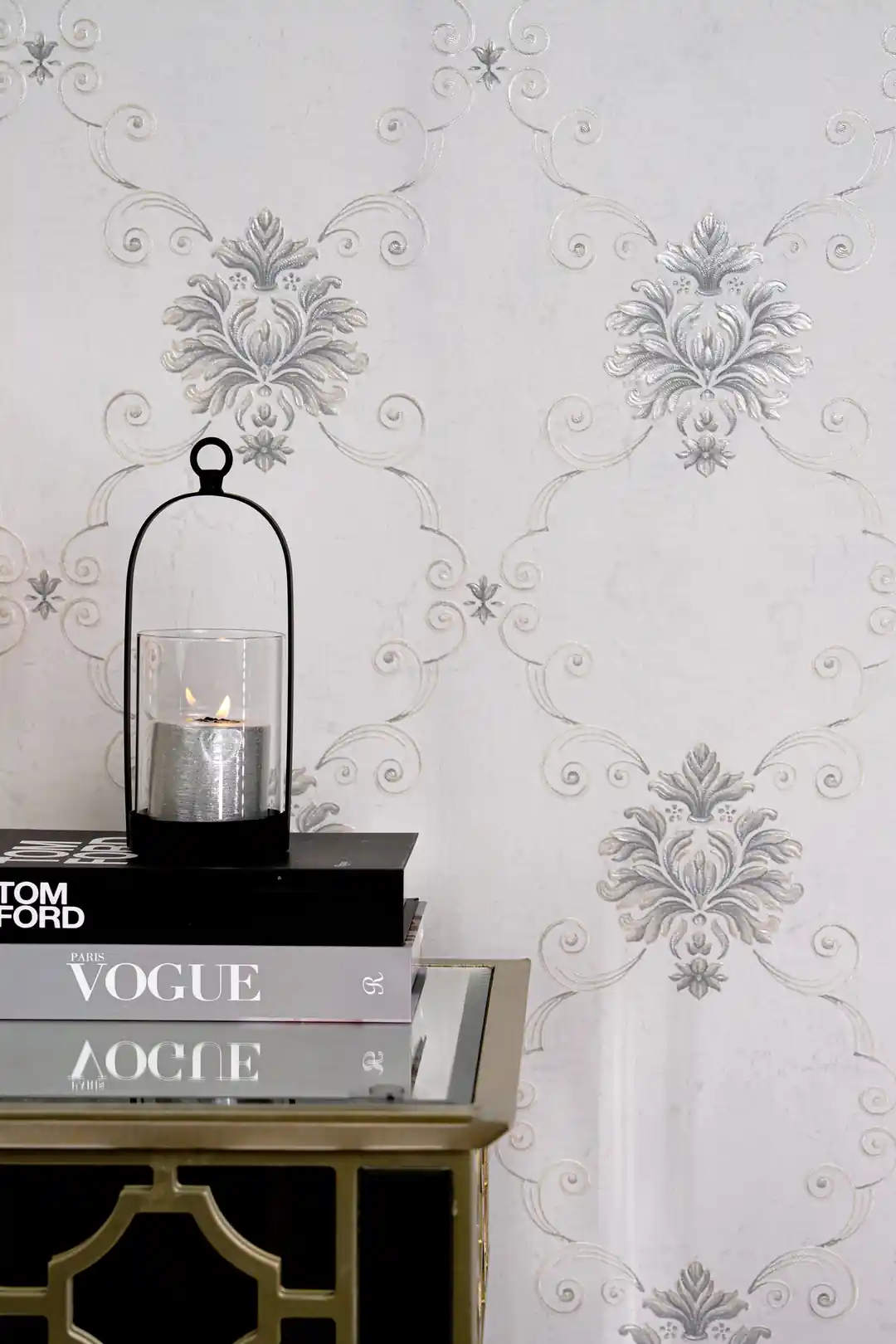 Installed wall showing embossed silver damask motifs with a candle lantern and fashion books on gold table