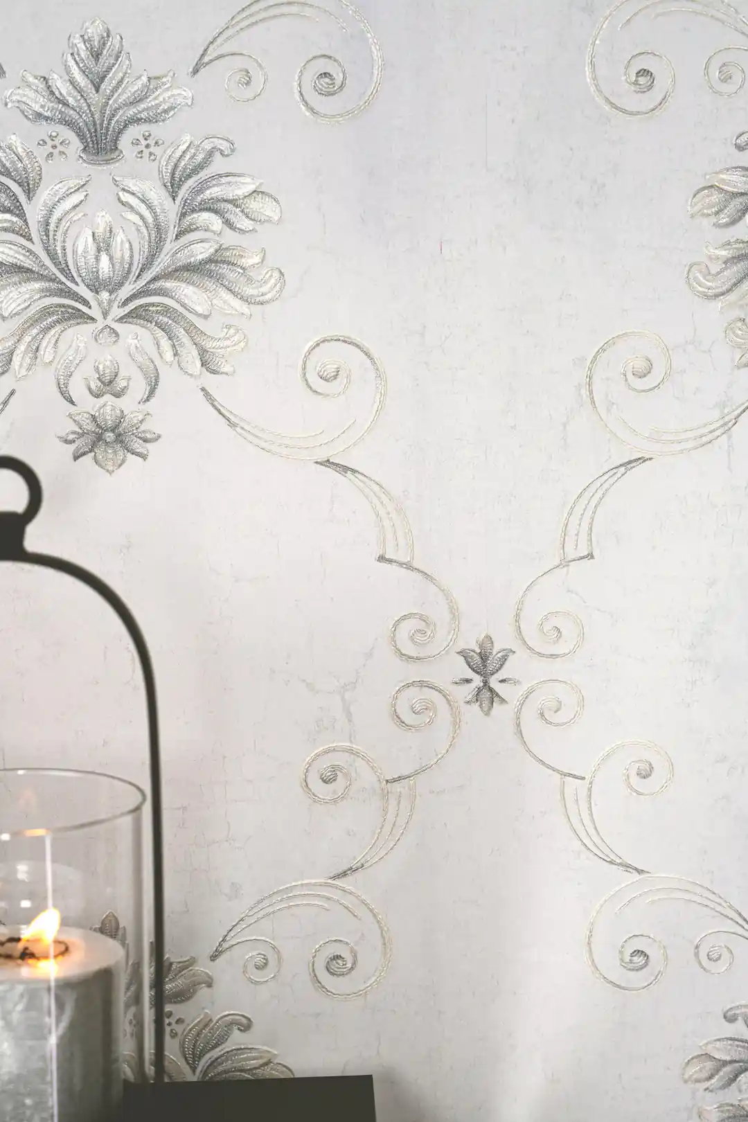 Close-up of silver damask scrollwork and floral medallion with a glass candle holder on grey wallpaper