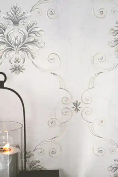 Close-up of silver damask scrollwork and floral medallion with a glass candle holder on grey wallpaper