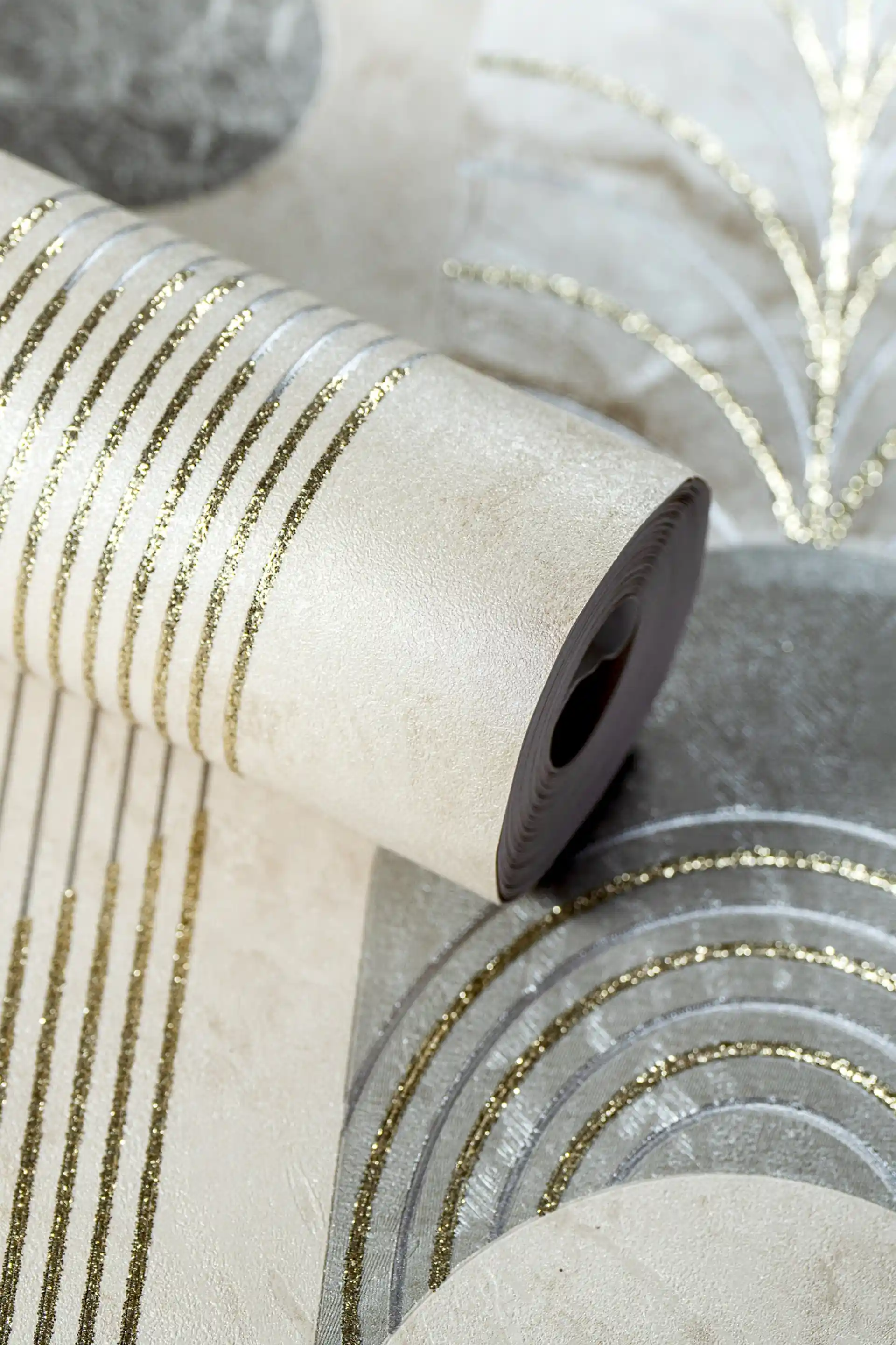 Rolled beige deco wallpaper with grey geometric arches, sunburst fan shapes, and gold glitter line accents on textured base