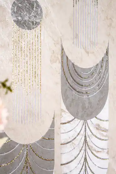 Detail of grey marble crescent shapes with gold glitter radiating lines on beige textured wallpaper surface