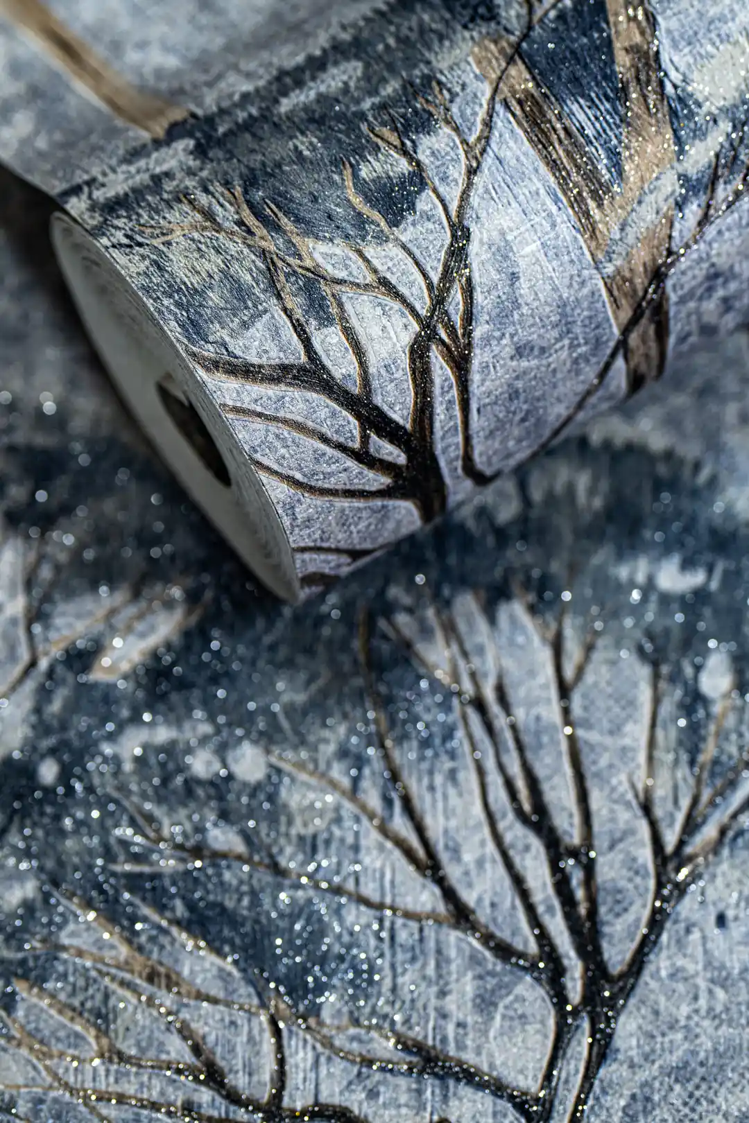 Rolled blue and grey misty forest wallpaper with tree silhouettes and glitter accents on textured base