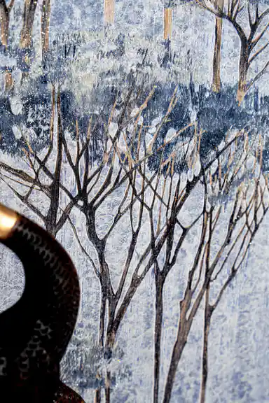 Detail shot of blue tree branches and canopy on misty grey wallpaper background with a dark decorative deer figurine