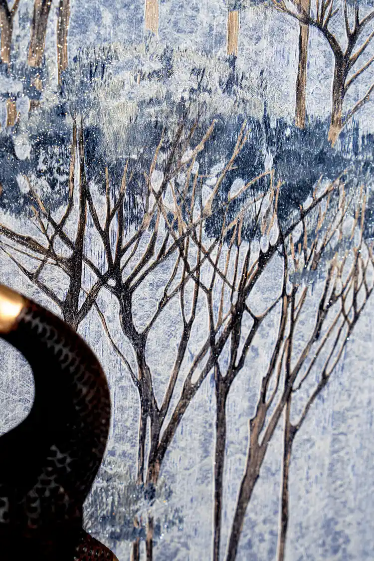 Detail shot of blue tree branches and canopy on misty grey wallpaper background with a dark decorative deer figurine