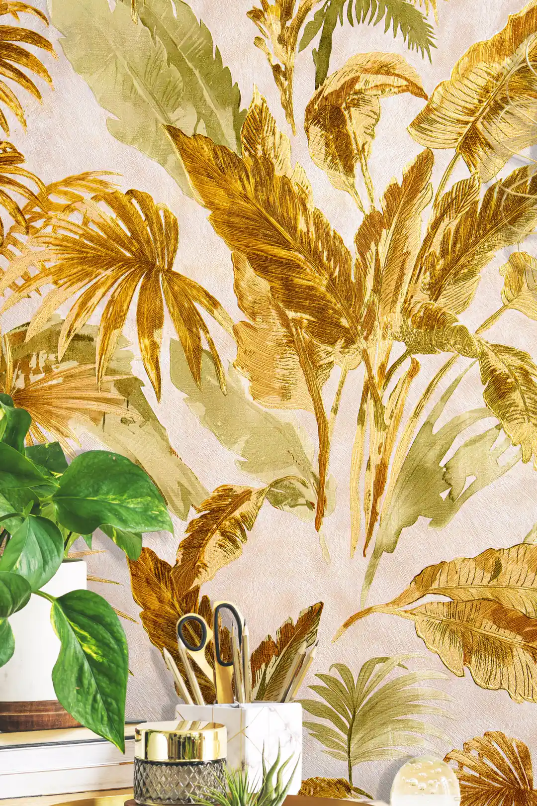 Installed wall close-up of gold and green tropical palm frond wallpaper with blurred houseplant in front