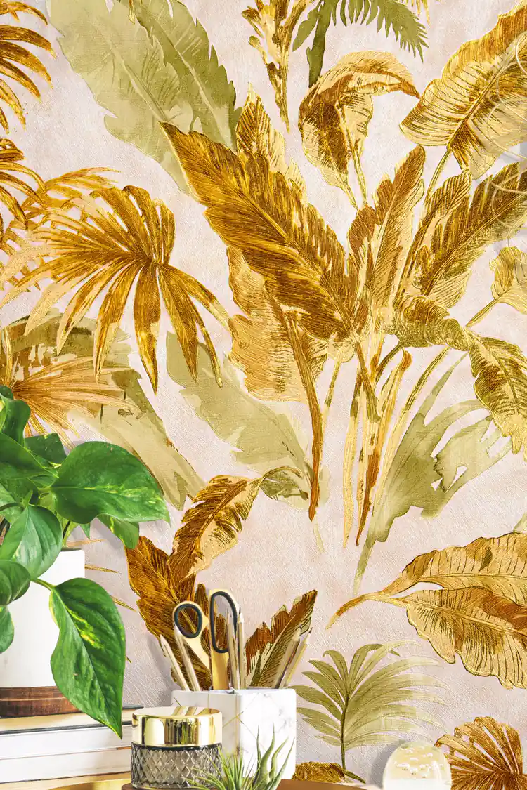 Installed wall close-up of gold and green tropical palm frond wallpaper with blurred houseplant in front
