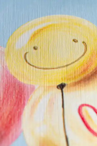 Extreme close-up of printed smiley face balloon and heart balloon detail on blue kids wallpaper texture