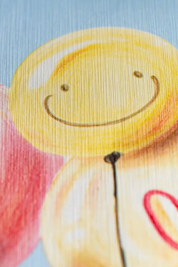 Extreme close-up of printed smiley face balloon and heart balloon detail on blue kids wallpaper texture