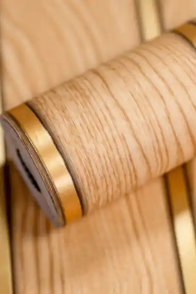 Oak wood slats wallpaper roll showing wood grain texture and golden metallic strip between the panels