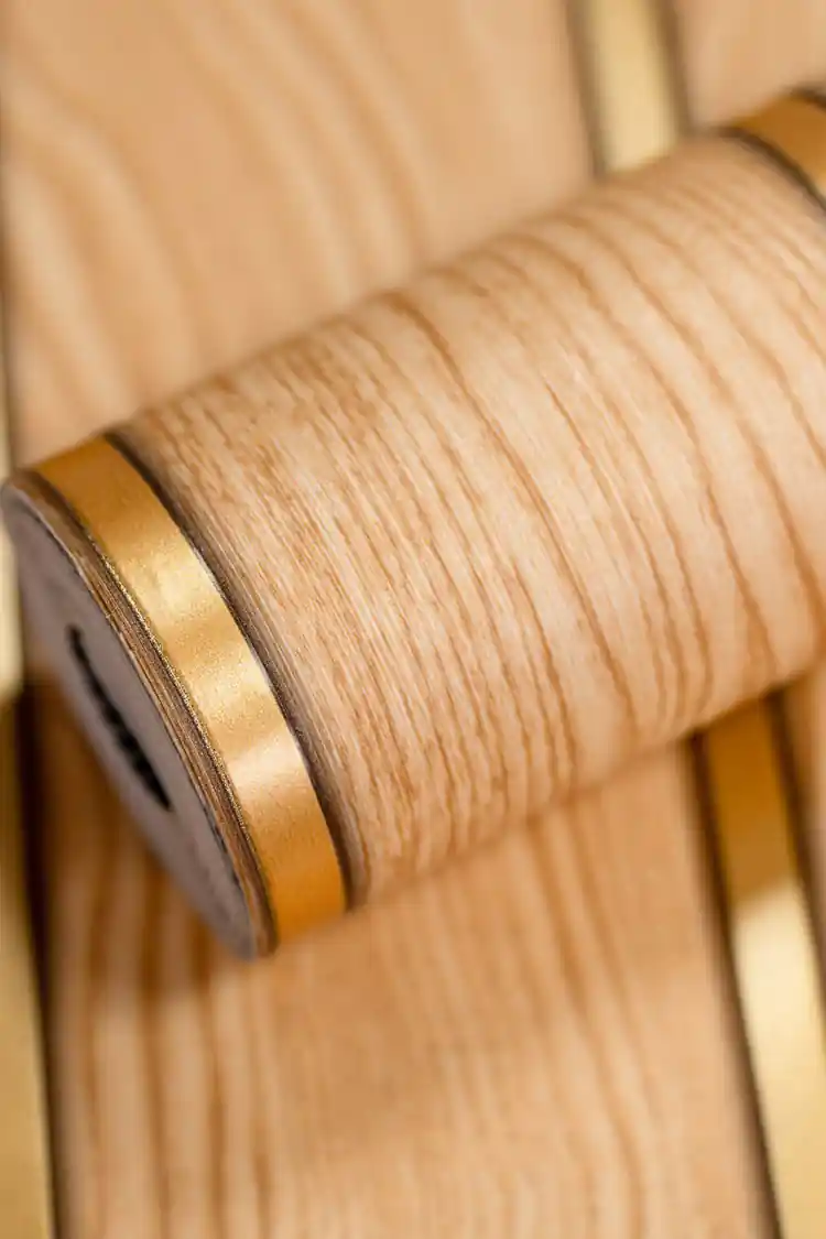 Oak wood slats wallpaper roll showing wood grain texture and golden metallic strip between the panels