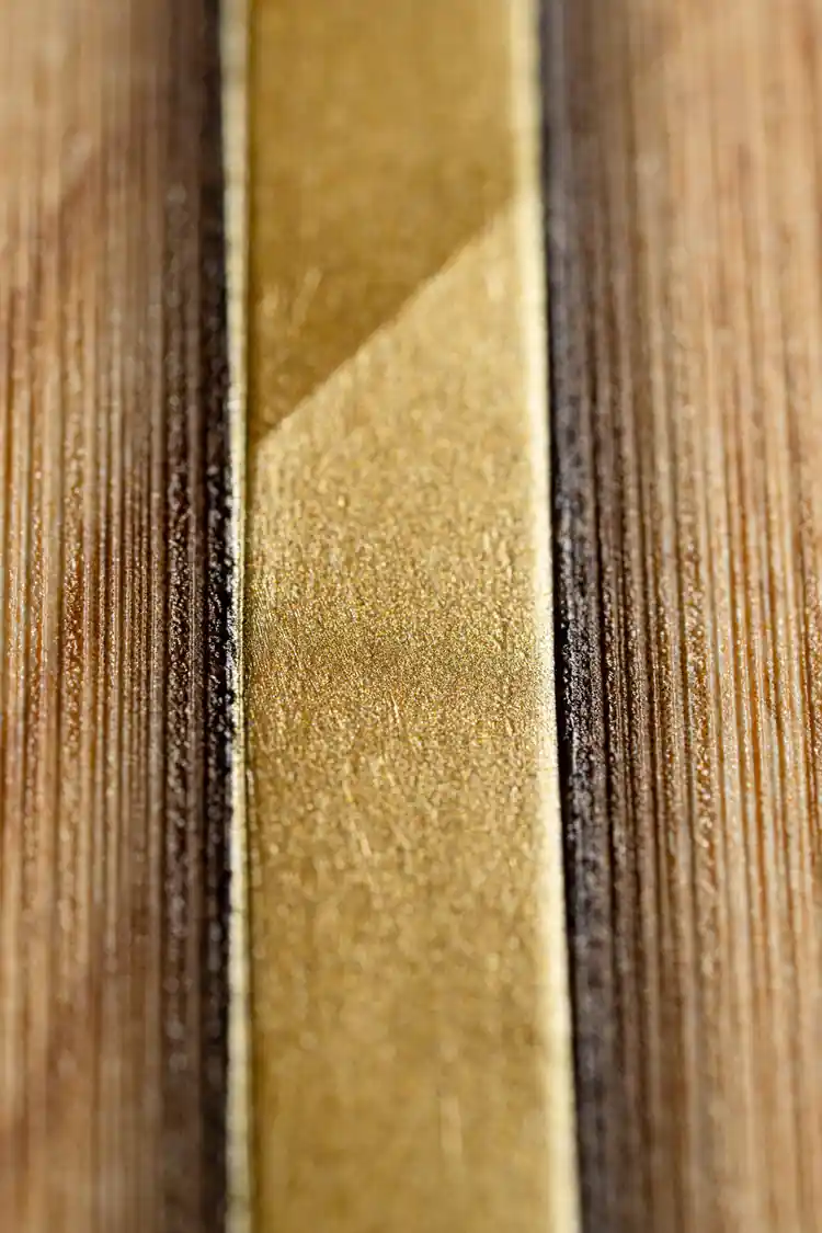 Extreme close-up macro of golden metallic strip line between two oak wood grain textured wallpaper slats