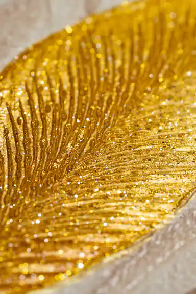 Extreme close-up macro of golden glitter leaf texture showing sparkling detail on beige wallpaper