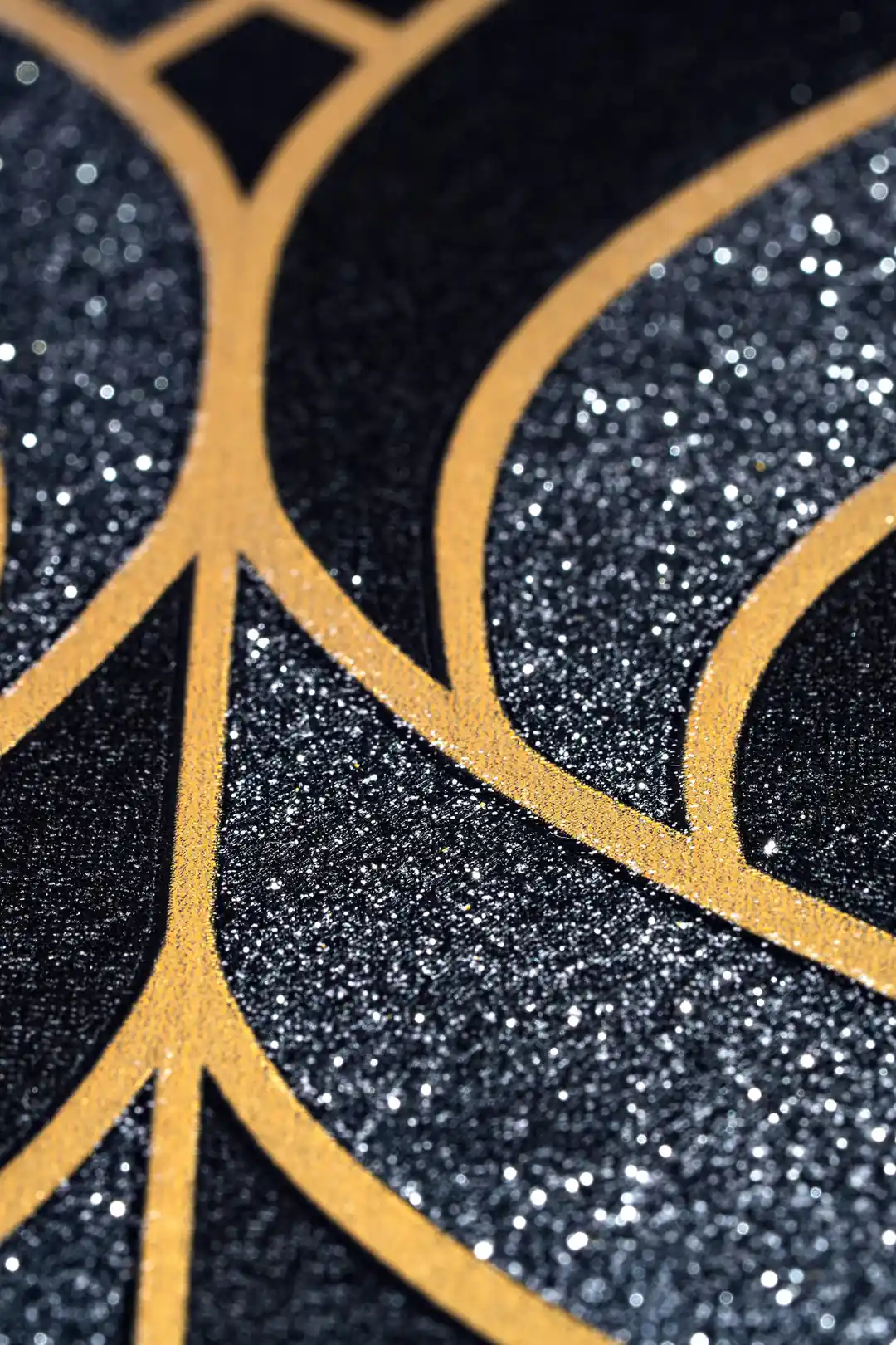 Extreme close-up of black wallpaper with gold leaf outline pattern showing glitter accent detail