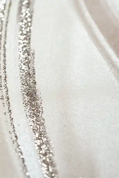 Extreme close-up macro of pearl silk wave wallpaper texture showing silver glitter particles along curved lines