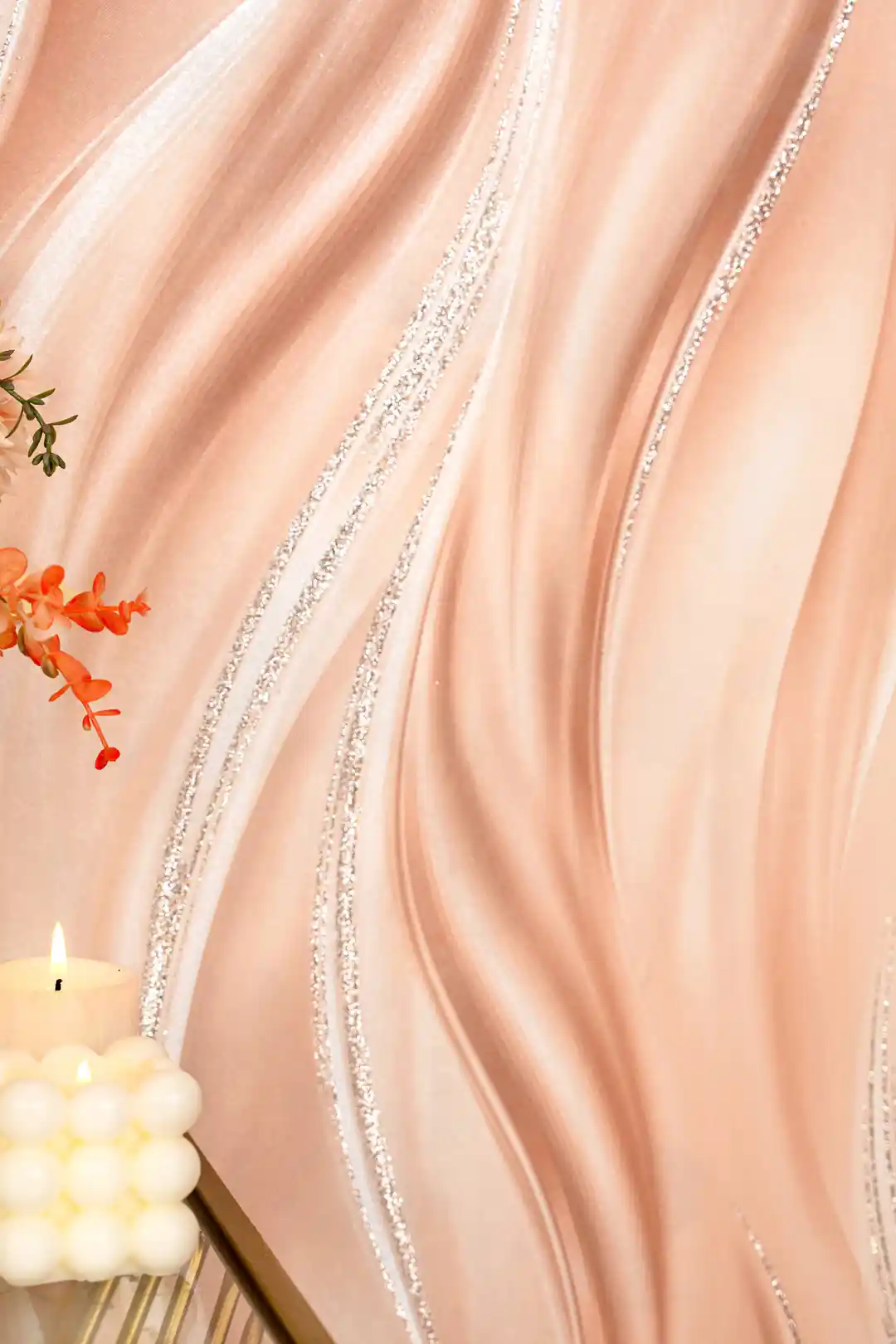 Close-up of peach silk wave wallpaper with silver glitter lines beside orange flowers and a candle
