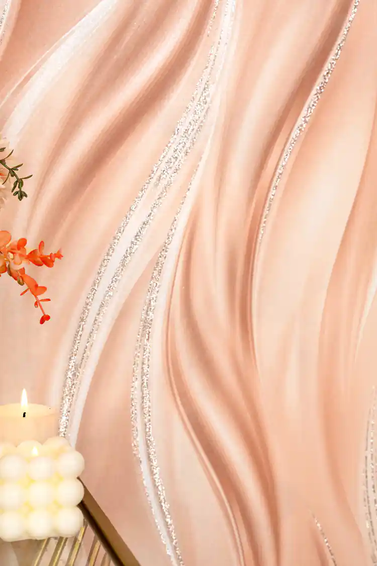 Close-up of peach silk wave wallpaper with silver glitter lines beside orange flowers and a candle