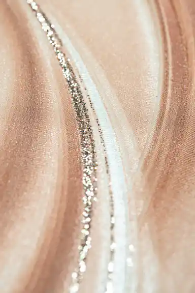 Extreme close-up macro of peach silk wave texture with silver glitter particles along curved line