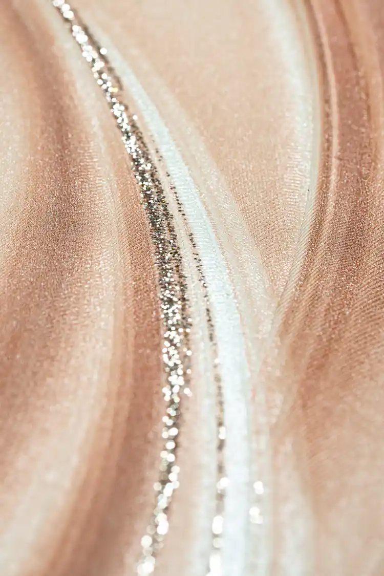 Extreme close-up macro of peach silk wave texture with silver glitter particles along curved line