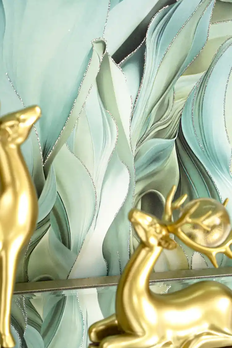 Close-up of green flowing leaf wallpaper with golden deer figurines on a glass shelf accent piece