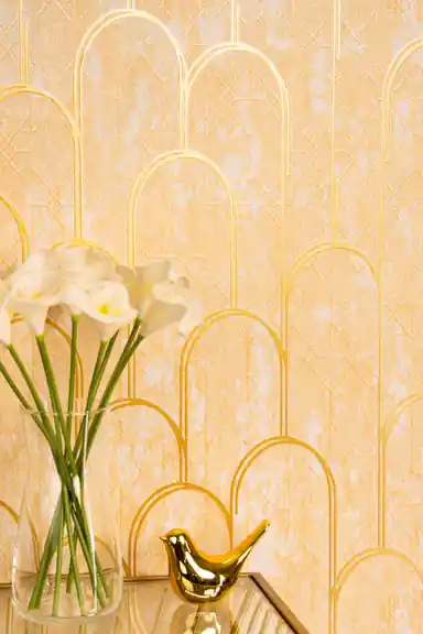 Close-up of gold art deco arch wallpaper with metallic gold lines beside white flowers in a vase and gold bird figurine
