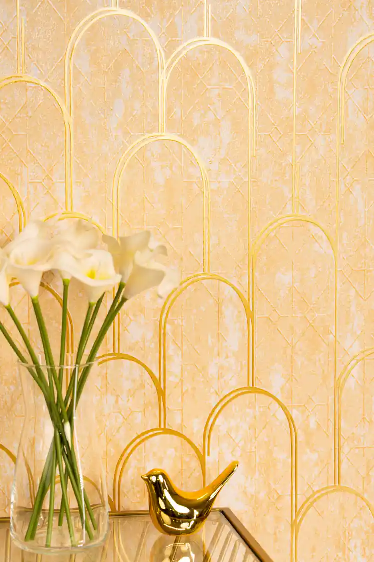 Close-up of gold art deco arch wallpaper with metallic gold lines beside white flowers in a vase and gold bird figurine