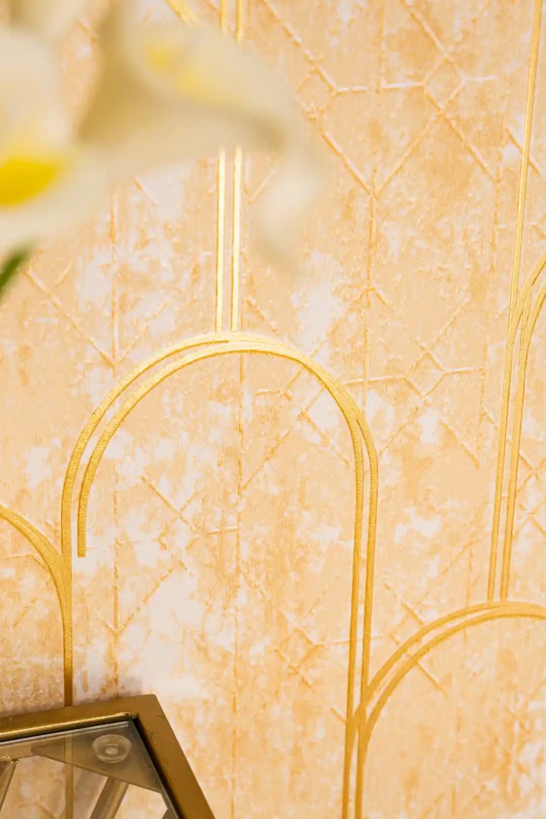 Detail of gold metallic arch lines on textured gold wallpaper surface with blurred glass accent below