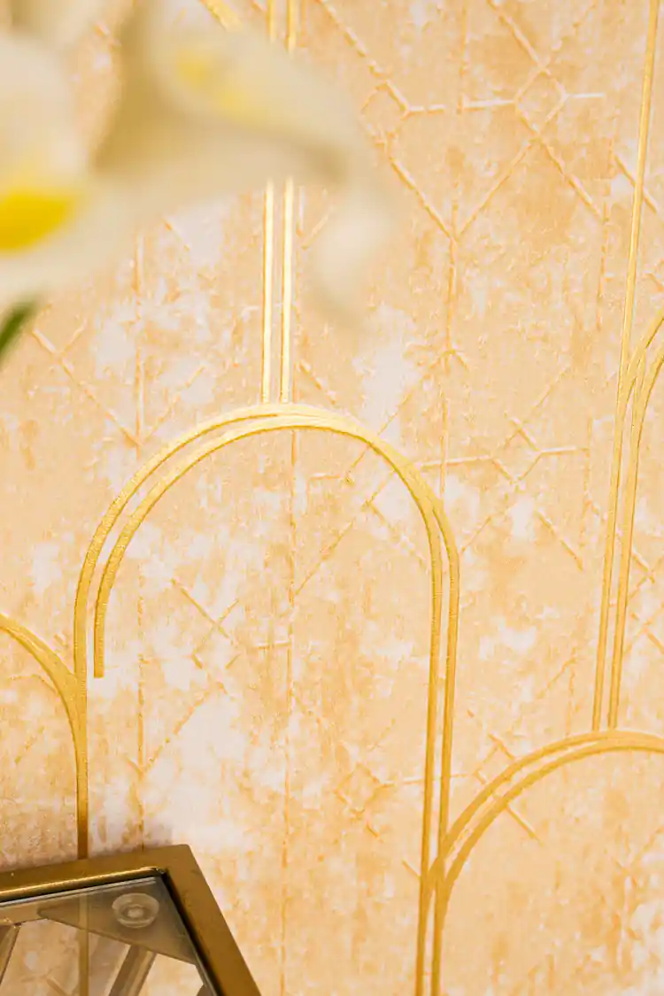 Detail of gold metallic arch lines on textured gold wallpaper surface with blurred glass accent below