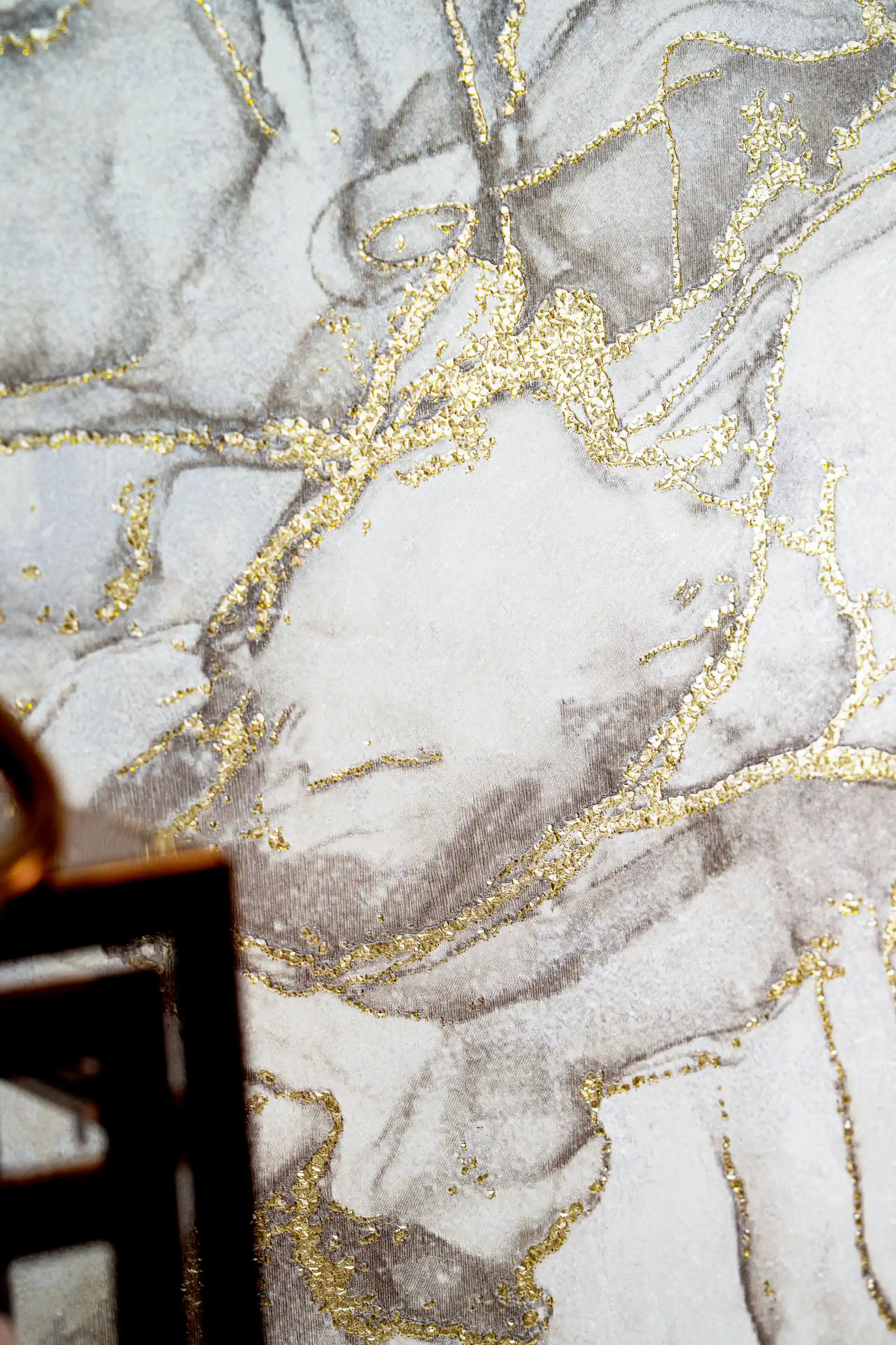 Close-up of grey marble wallpaper with sparkling metallic gold vein accents on an installed wall
