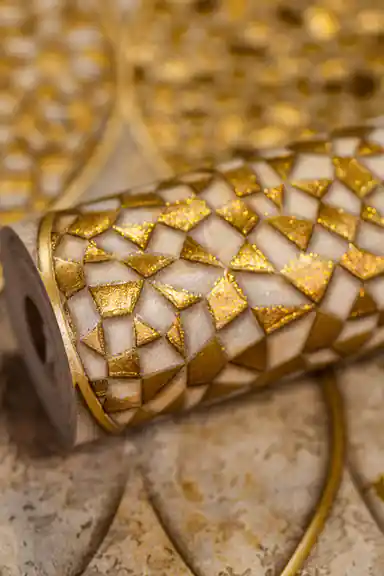 Rolled wallpaper displaying geometric gold mosaic tile pattern with glitter on a textured beige base