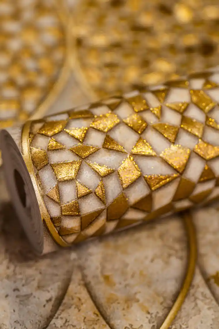 Rolled wallpaper displaying geometric gold mosaic tile pattern with glitter on a textured beige base