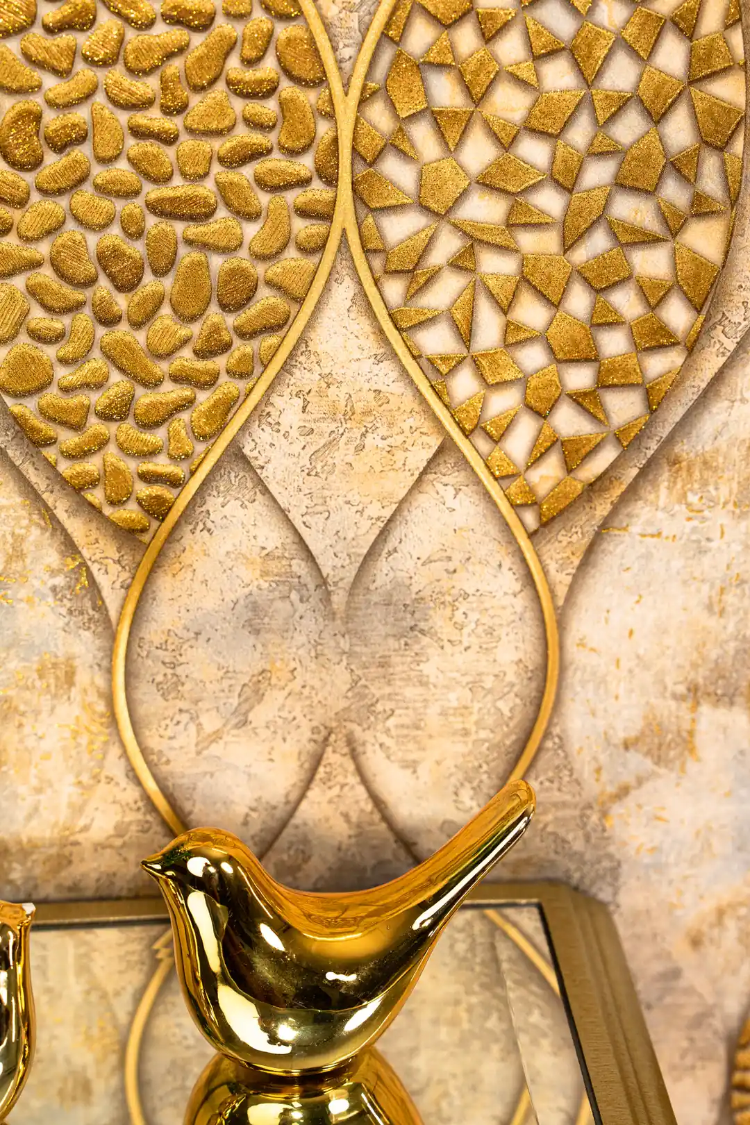 Detail shot of raised gold pebble and triangle mosaic textures within the wave-outlined leaf shapes with gold bird figurine in foreground