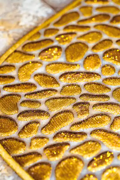 Macro close-up of glittering gold pebble-shaped embossed elements on the beige wallpaper surface
