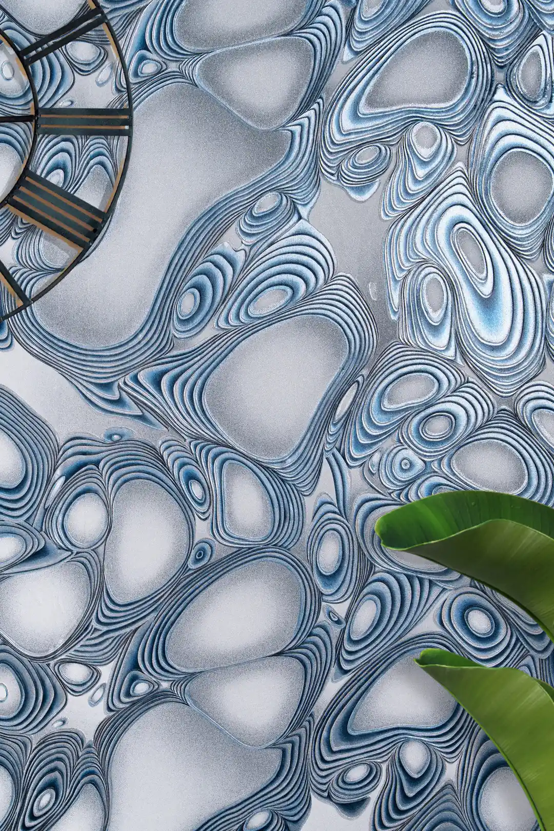 Overhead styled view of blue metallic swirl wallpaper with a wall clock and tropical leaf