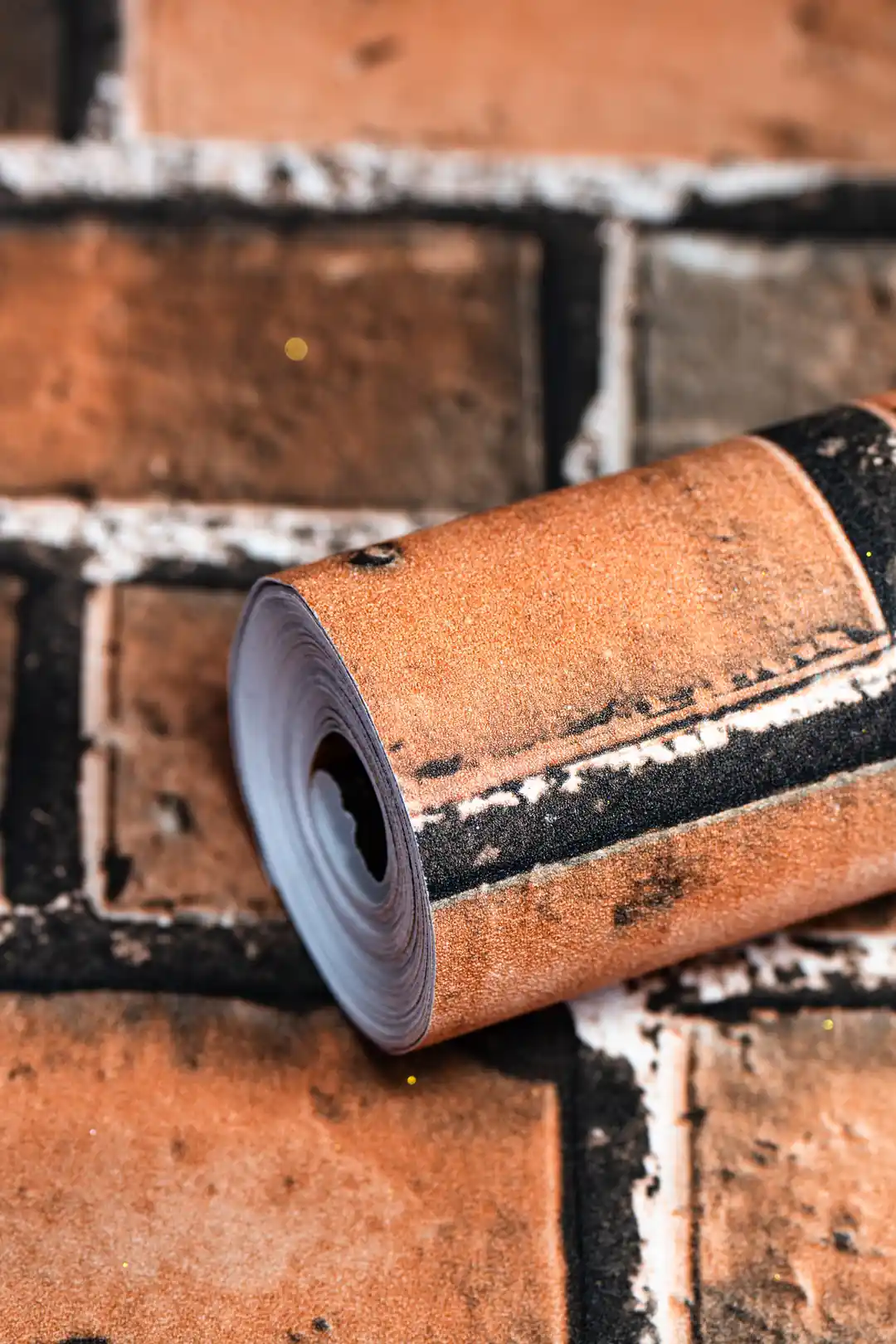 Rolled rustic red brick pattern wallpaper resting on the matching brick-textured unrolled surface