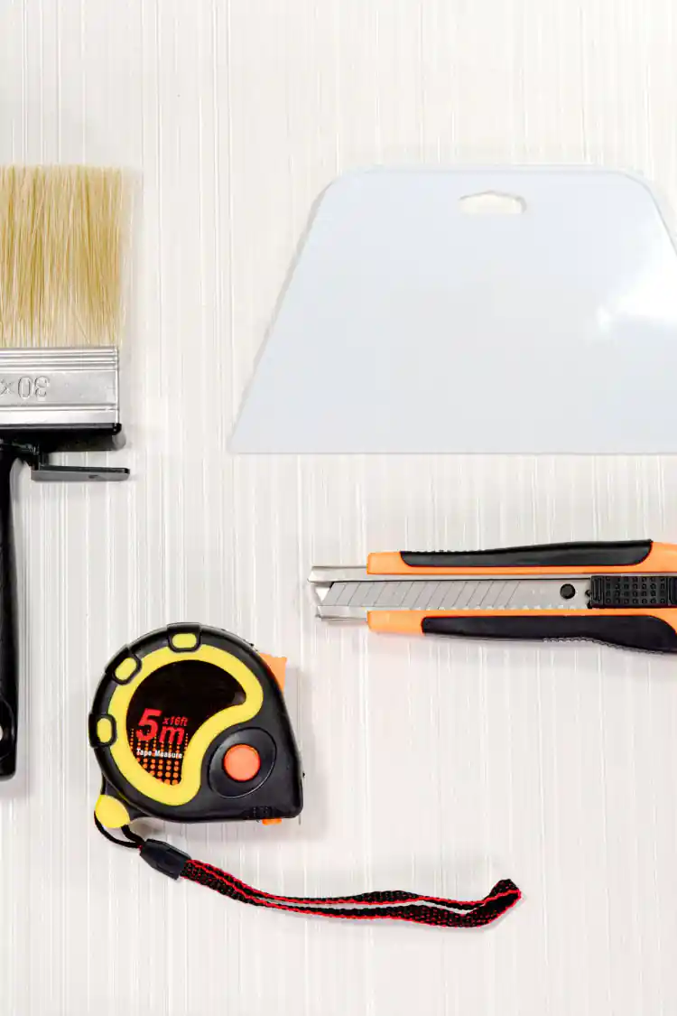 Flat lay of complete wallpaper tool kit showing brush, squeegee, knife, and 5m tape measure